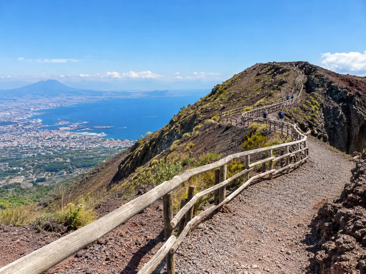 Il sentiero di ghiaia a tornanti con recinzioni di legno che sale sul cono del Vesuvio sopra il Golfo di Napoli